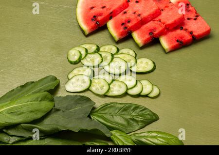 Spinach leaves, sliced cucumbers and watermelon wedges. Top view. Green background. Stock Photo