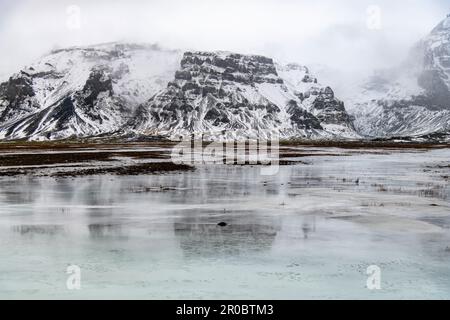 Low angle view of mountain range in low hanging clouds with black and white pattern of rock and snow on slopes at the end of the Orafajokull volcano Stock Photo