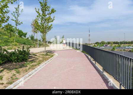 A person jogging on a walkway with red brick pavement and metal railing in a new urban park Stock Photo