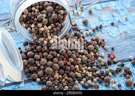 Kernels of various types of volcanic peppers from a jar on a blue table Stock Photo