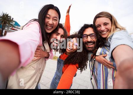 Happy group of friends having fun outdoors, doing piggyback while taking a selfie for social media. Stock Photo