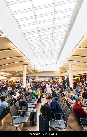 Heathrow airport, terminal three. Interior of the busy main departure lounge crowded with people sitting and walking around waiting for flights. Stock Photo