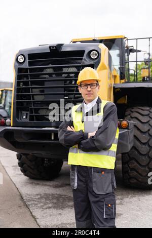 Engineer in a helmet with a digital tablet on the background of construction machine. High quality photo Stock Photo