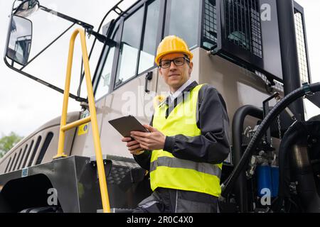 Engineer with tablet computer stands on the stairs to the cab of a truck. High quality photo Stock Photo