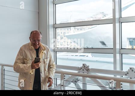 middle age bald man taking photo with smart phone in waiting room at port - Happy tourist traveling by cruise ship - Tourism and vacations concept Stock Photo