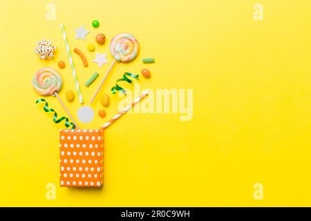 gift box in corner full of assorted traditional candies falling out on colored background with copy space. Happy Holidays sale concept. Stock Photo