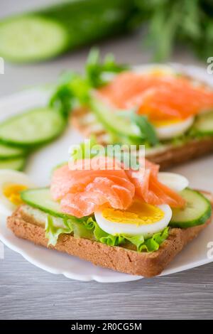 fried toast with lettuce, egg, cucumbers and red fish in a plate, on a wooden table. Stock Photo