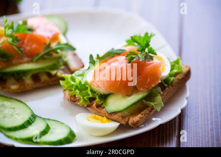fried toast with lettuce, egg, cucumbers and red fish in a plate, on a wooden table. Stock Photo