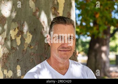 A handsome man leaning on a tree and looking at the camera Stock Photo