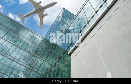 Airplane flying above modern office building. Exterior facade of skyscraper green glass building. Business trip. Reflection in transparent glass Stock Photo