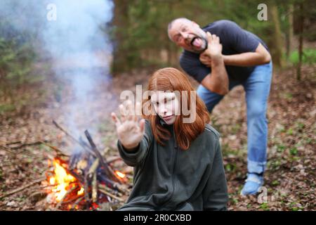 A young red-haired witch with a magic hand and a a old man on a back start to die of curse Stock Photo