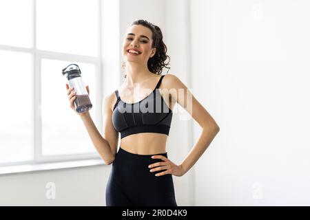 Sporty girl drinking water after workout. Photo of latin fitness girl on grey background. Healthy lifestyle Stock Photo