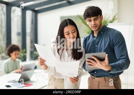 Diverse Business Colleagues Using Digital Tablet Holding Papers In Office Stock Photo