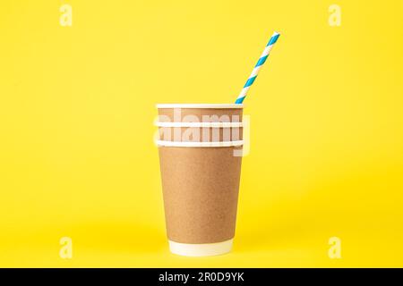 Three paper disposable cups and a striped paper straw on a yellow background. Stock Photo