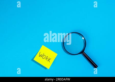 Magnifying loupe and a sticker with the word work on a blue background. Stock Photo