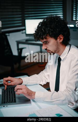 Concentrated entrepreneur working on laptop at his office desk late at night Stock Photo