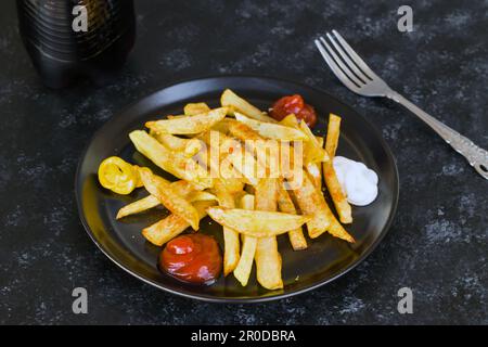 French fries designed with ketchup, mayonnaise and mustard sauce on a black plate Stock Photo