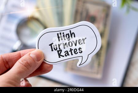 Top view of trash paper, paper clip, calculator, pen and white sticky notes written with High Turnover Rates in hand. Stock Photo
