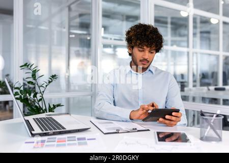 Serious thinking hispanic businessman working with documents and invoices inside office, man behind paper work, using laptop at work sitting at desk. Stock Photo