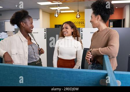 Three young diverse female colleagues stand and chat in open plan office Stock Photo