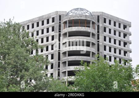 Concrete building framed by green trees isolated on clean sky Stock Photo