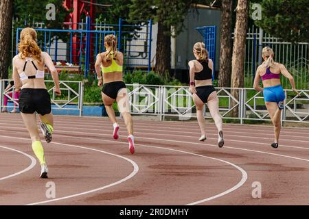 rear view four women athletes runners running sprint race in summer athletics championships Stock Photo