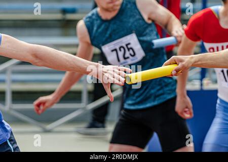 men relay race baton passing in summer athletics championship, close-up of athletes hands on background of runners Stock Photo