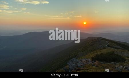 Sunrise in mountains. Natural mountain landscape with illuminated misty peaks, foggy slopes and valleys, blue sky with orange yellow sunlight. Amazing Stock Photo