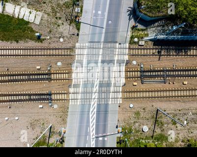 Railroad level crossing with half closed barriers. Railway tracks with concrete ties and switch panels on gravel. Aerial view from above Stock Photo