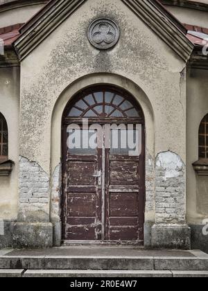 Old weathered wooden double door with arched window on a historic building facade, showing cracked plaster, aged masonry and traditional architectural Stock Photo