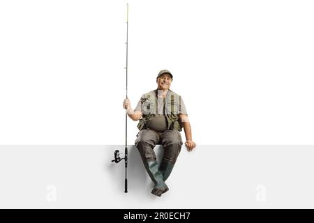 Mature fisherman with a fishing rod sitting on a blank panel isolated on white background Stock Photo