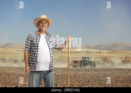 Mature farmer holding a shovel and posing with a pile of burlap sacks ...