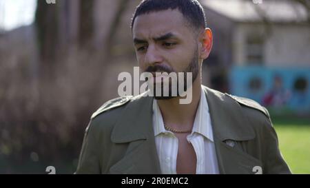One thoughtful young Middle Eastern man standing outside at park thinking. Closeup face of a pensive Arab male person Stock Photo