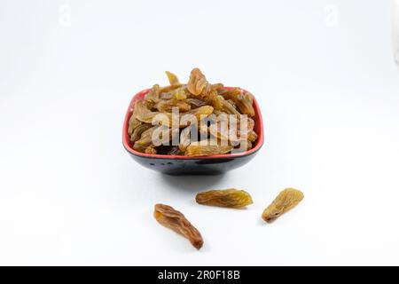 A close-up of a red bowl filled with dried raisins against a white background Stock Photo