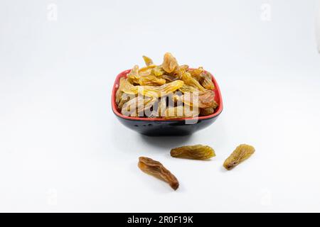 A close-up of a red bowl filled with dried raisins against a white background Stock Photo