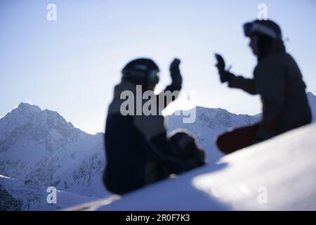 Young man and woman sitting on snow, clapping hands, Kuehtai, Tyrol, Austria Stock Photo