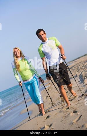 Couple walking with poles on beach, Apulia, Italy Stock Photo