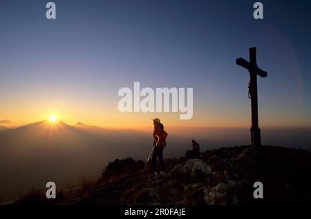 Mountaineer and cross on the summit of Heuberg with sunset over the Wendelstein range, Bavarian Alps, Upper Bavaria, Bavaria, Germany Stock Photo