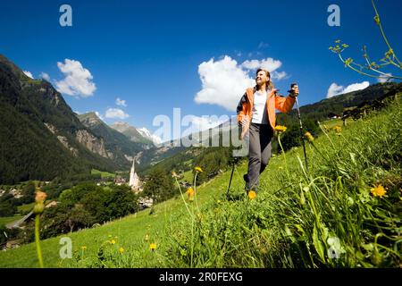 Woman hiking over alp above Heiligenblut with pilgrimage church Zum heiligen Blut, view to Grossglockner, Heiligenblut, Carinthia, Austria Stock Photo