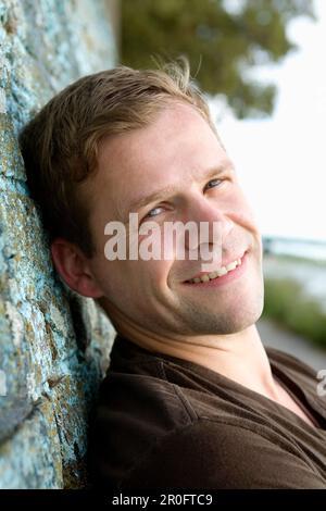 Mid adult man looking at camera while leaning against a wall, Duesseldorf, North Rhine-Westphalia, Germany, Düsseldorf, North Rhine-Westphalia, German Stock Photo