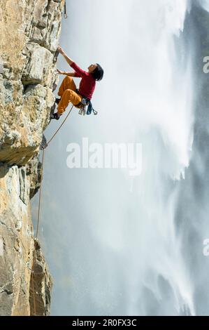 Female free climber scaling rock face, Fallbach Waterfall in background, Malta Valley, Hohe Tauern National Park, Carinthia, Austria Stock Photo