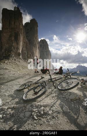 Three persons resting, mountain bikes in foreground, Tre Cime di Lavaredo, Veneto, Italy Stock Photo