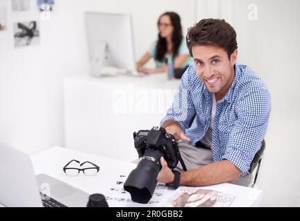 Using the tools of the trade. Two photographers sitting in their office working on layouts and inspecting their equipment. Stock Photo