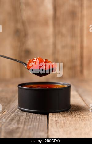 Red salmon caviar in a black tin can and a black spoon full of caviar on a wooden background. Healthy seafood. Stock Photo