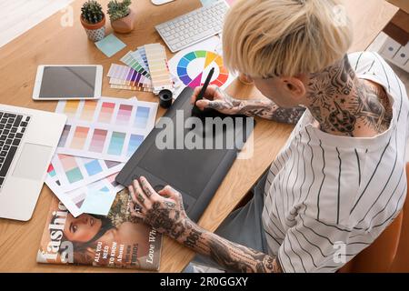Tattooed graphic designer working with tablet on table in office, closeup Stock Photo