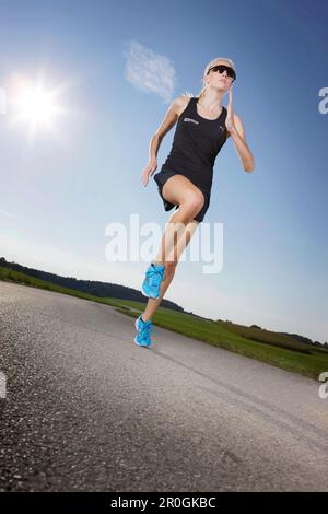 Female runner on road near Munsing, Upper Bavaria, Germany Stock Photo