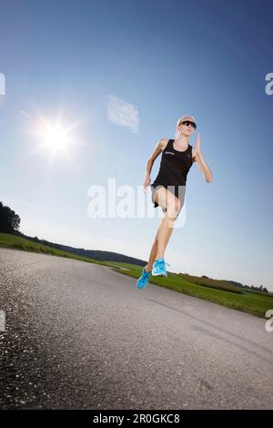 Female runner on road near Munsing, Upper Bavaria, Germany Stock Photo