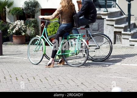 Young couple on bicycles standing talking on the streets, Amsterdam, Netherlands Stock Photo