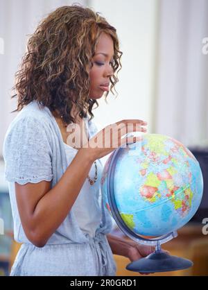 You can always learn something new about the world. A young teacher holding a globe of the world during geography. Stock Photo