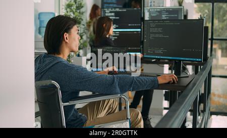 Focused software developer in wheelchair writing server code in agency data room, using security system. Engineer with physical disability programming user interface artificial intelligence office. Stock Photo